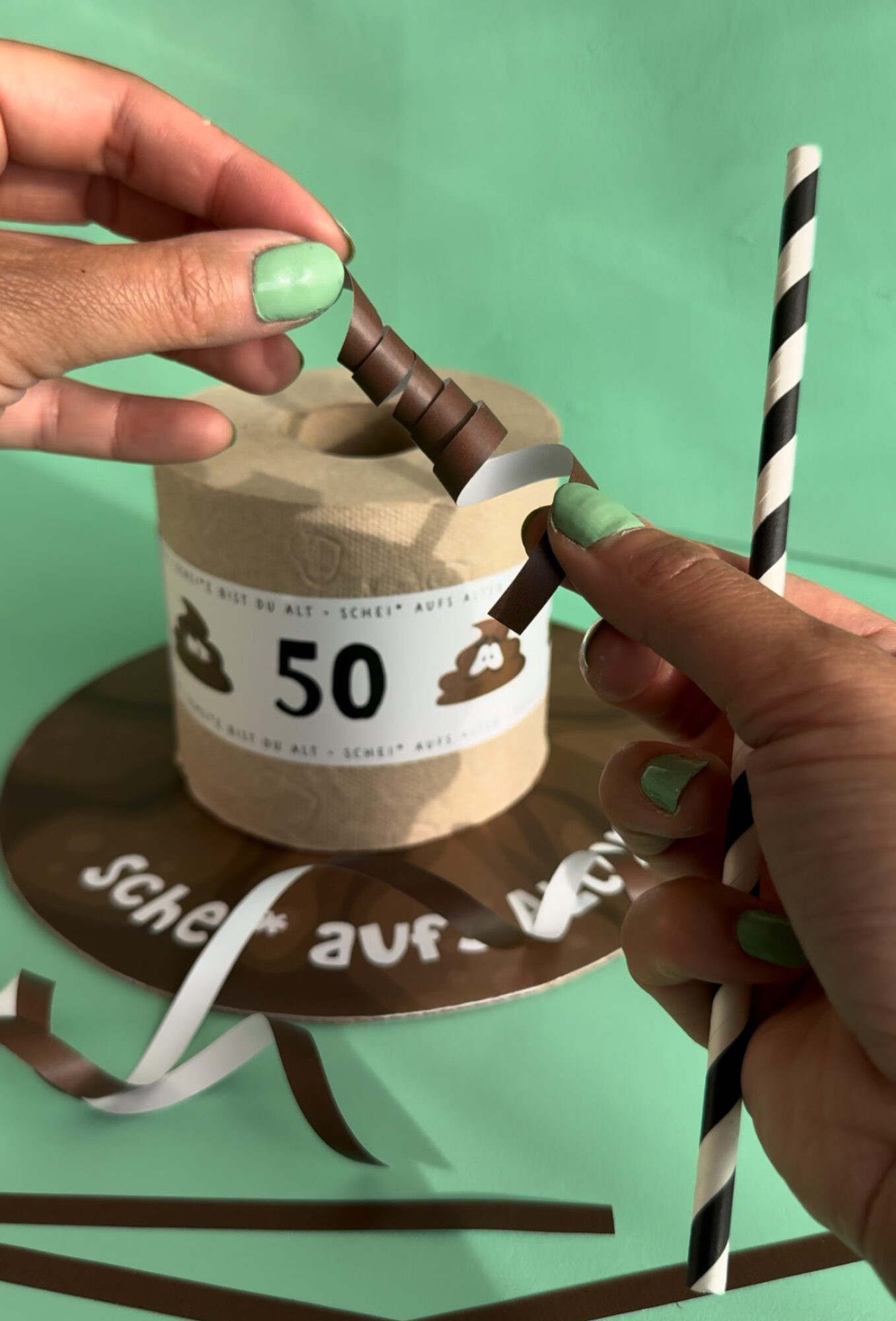 Witziges Geldgeschenk zum 50. Geburtstag als Klorolle mit Banderole, Kackhaufen mit Wackelaugen, Geldschein Kerzen und Schild Alles Gute zum 50. Geburtstag, mintgrüner Hintergrund