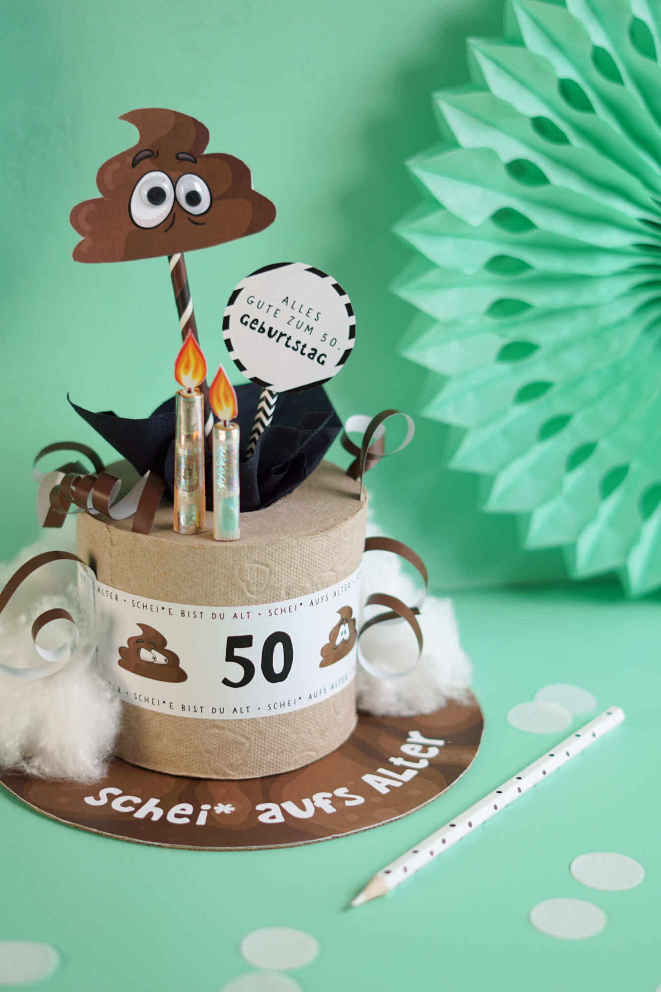 Witziges Geldgeschenk zum 50. Geburtstag als Klorolle mit Banderole, Kackhaufen mit Wackelaugen, Geldschein Kerzen und Schild Alles Gute zum 50. Geburtstag, mintgrüner Hintergrund