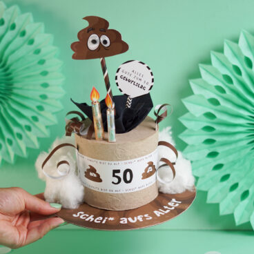 Witziges Geldgeschenk zum 50. Geburtstag als Klorolle mit Banderole, Kackhaufen mit Wackelaugen, Geldschein Kerzen und Schild Alles Gute zum 50. Geburtstag, mintgrüner Hintergrund