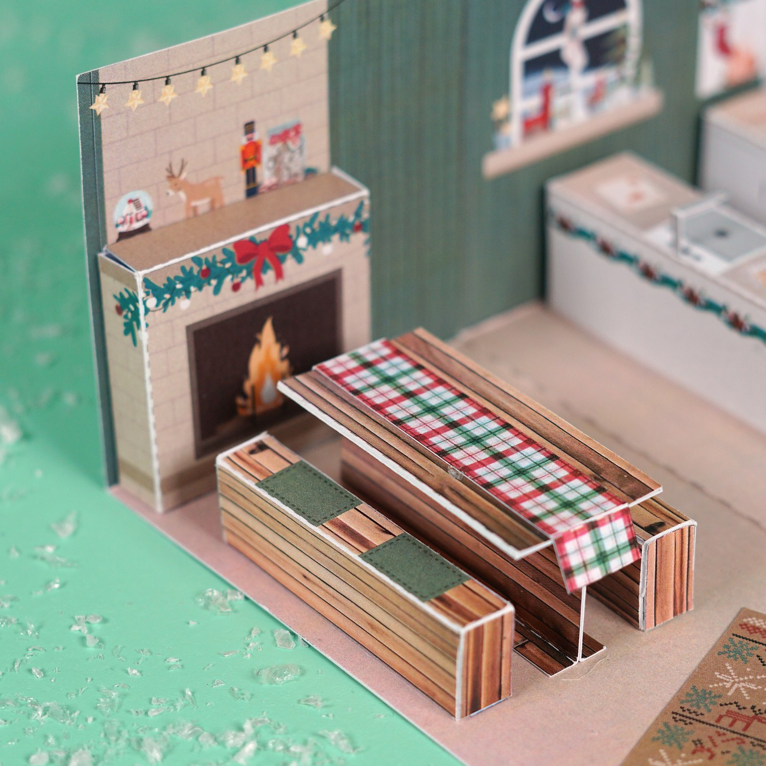 Kamin mit Tannengirlande und Nussknacker, davor Holztisch mit karierter Tischdecke in der Weihnachtsbäckerei aus Papier