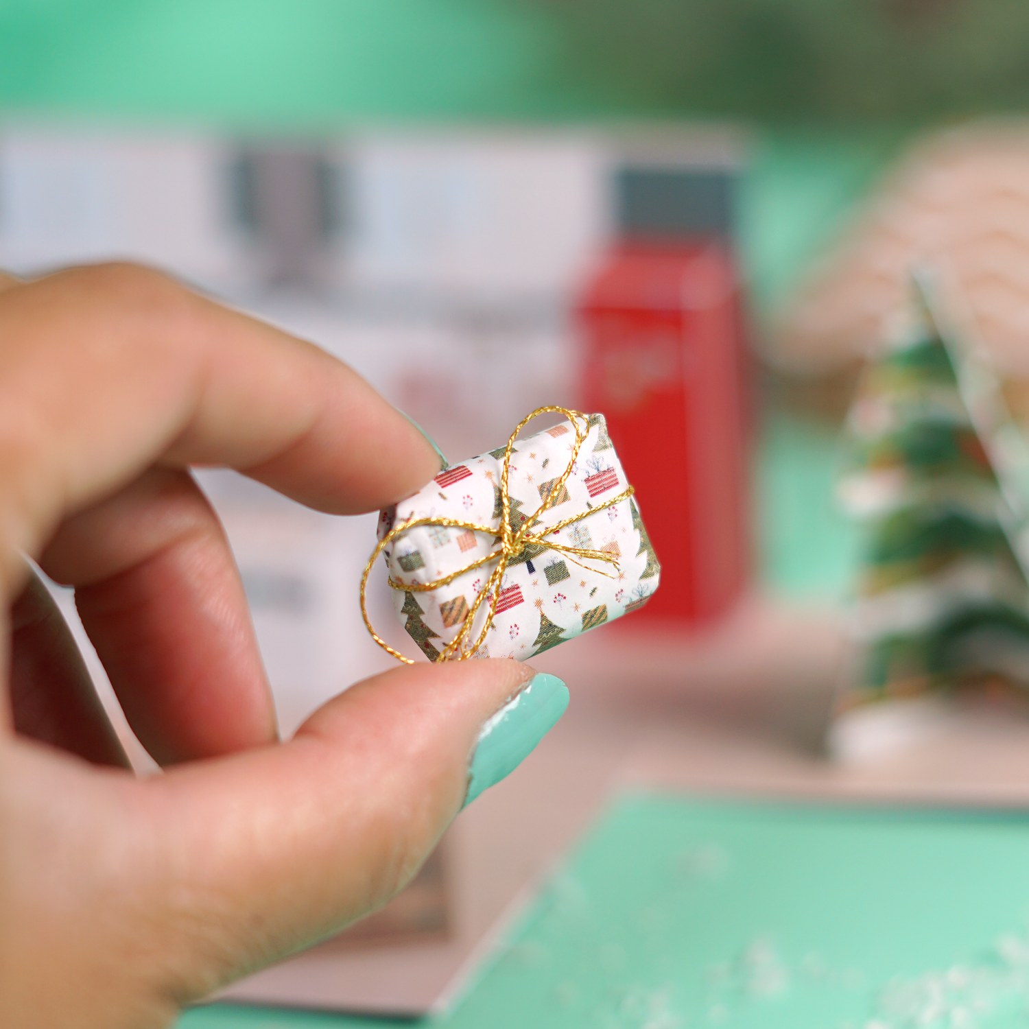 Mini Geschenk mit gefaltetem Geldschein zwischen zwei Fingern vor dem Tannenbaum aus Papier