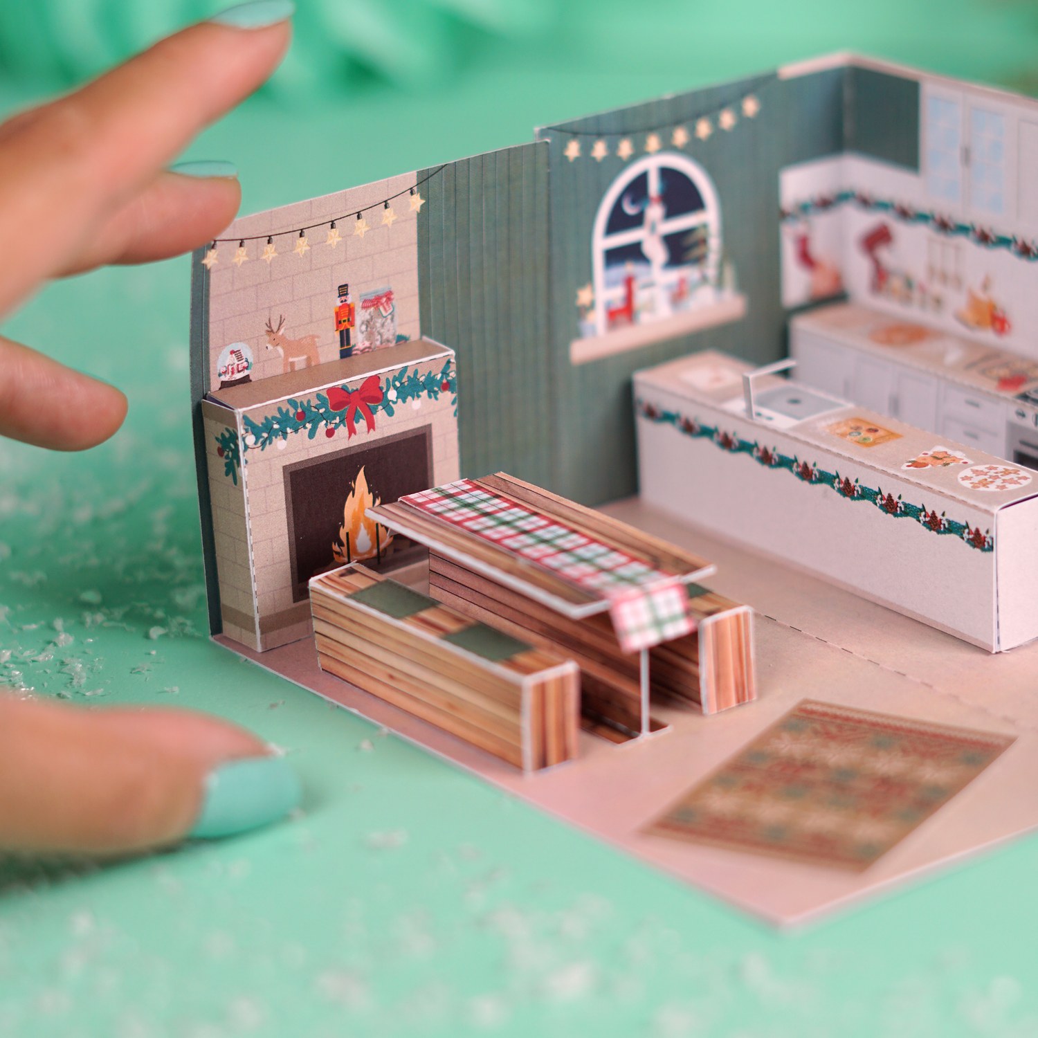 Hand öffnet die Lebkuchenhaus Explosionsbox, darin eine Weihnachtsbäckerei mit Kamin und Tisch