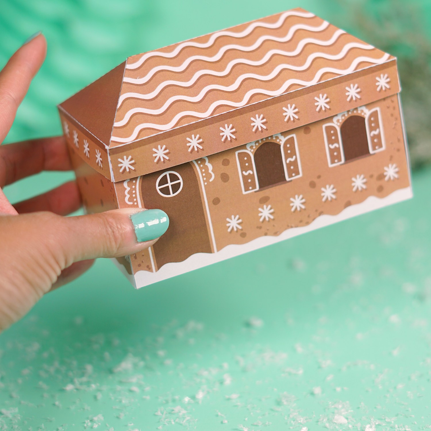 Hand hält das geschlossene Lebkuchenhaus mit Zuckergussdach, DIY Geldgeschenk zu Weihnachten