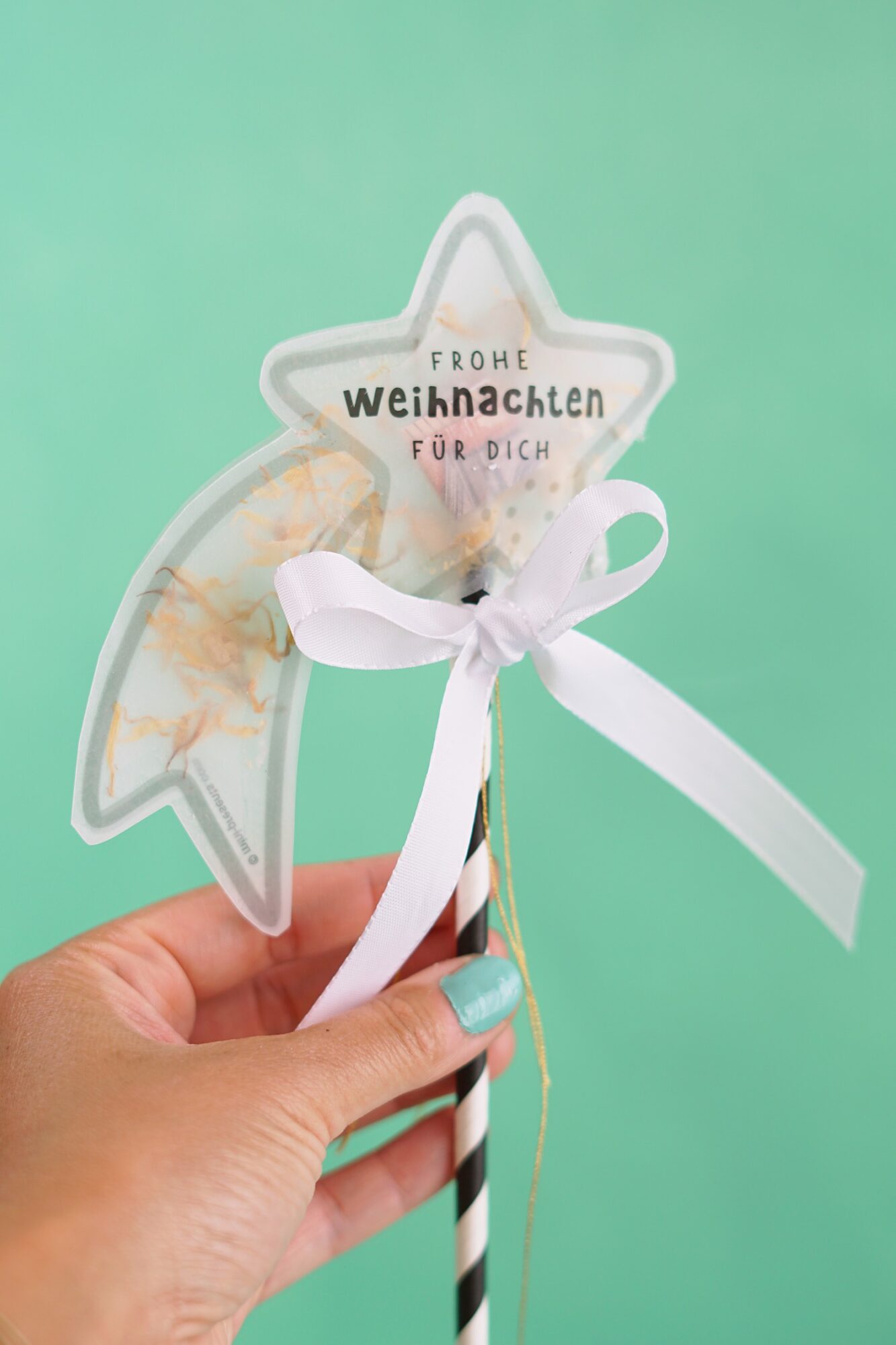 Hand hält die Sternschnuppe am Stab mit weißer Schleife, Konfettikarte Frohe Weihnachten für dich