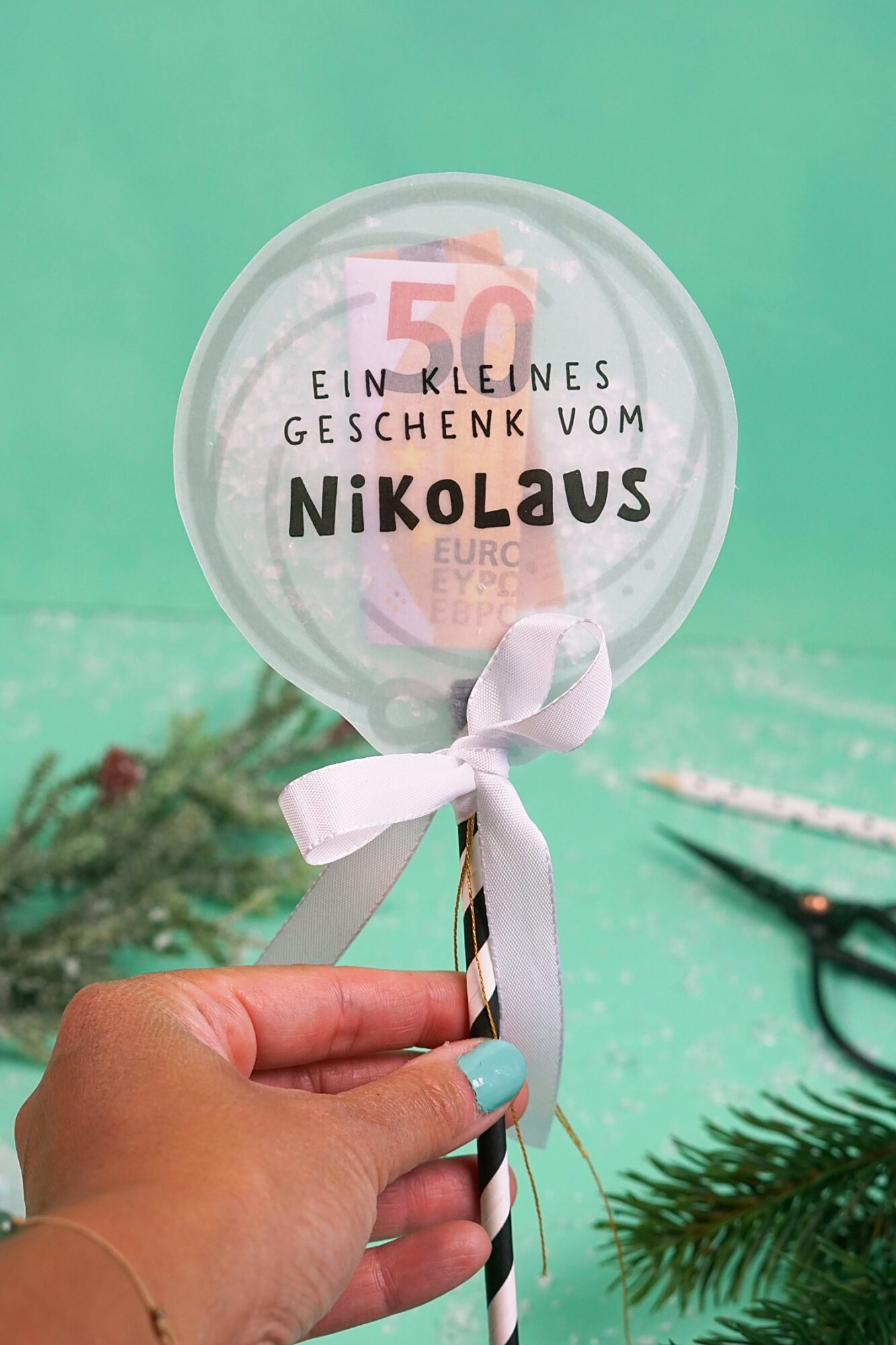 Hand hält den Lutscher am Stab mit Schleife, Konfettikarte Ein kleines Geschenk vom Nikolaus
